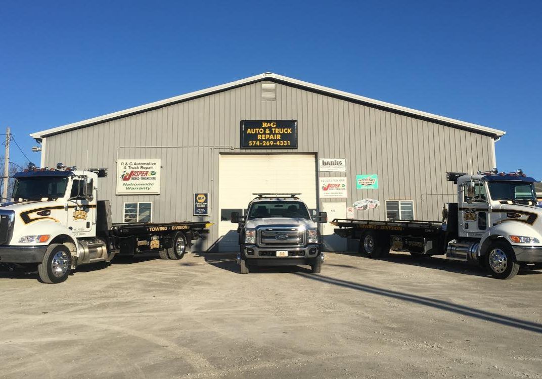 R&G Auto & Truck Repair shop building with two flatbed tow trucks and a service truck parked out front